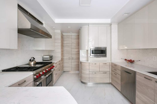 kitchen with light stone countertops, white cabinetry, appliances with stainless steel finishes, and wall chimney exhaust hood