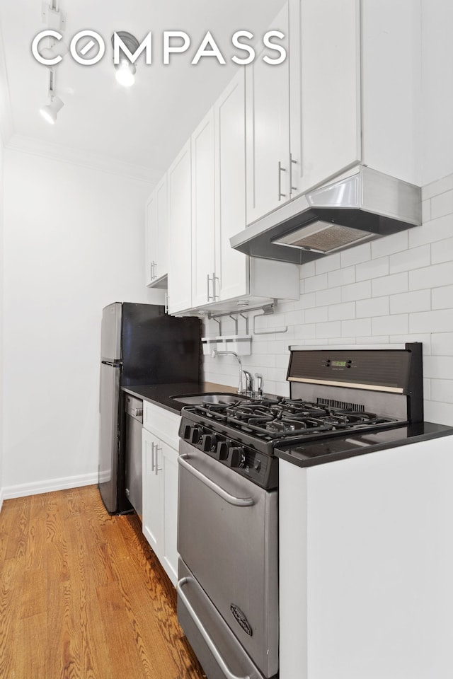 kitchen featuring dark countertops, tasteful backsplash, under cabinet range hood, stainless steel appliances, and white cabinetry