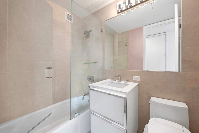 full bathroom featuring tile walls, vanity, enclosed tub / shower combo, and toilet