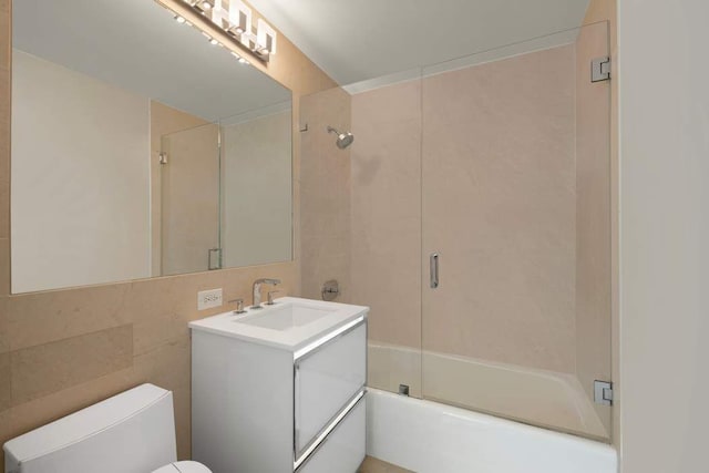 full bathroom featuring vanity, combined bath / shower with glass door, tile walls, and toilet