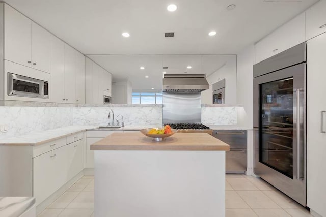 kitchen with appliances with stainless steel finishes, range hood, sink, white cabinets, and a center island