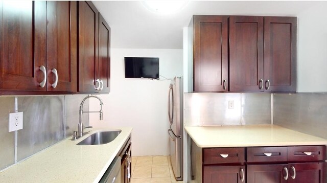 kitchen with decorative backsplash, freestanding refrigerator, light tile patterned flooring, a sink, and dark brown cabinets