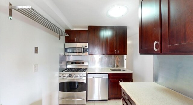 kitchen featuring decorative backsplash, stainless steel appliances, dark brown cabinets, light countertops, and a sink