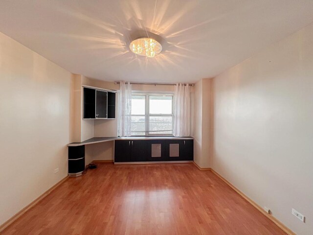 empty room with light wood-type flooring and a chandelier