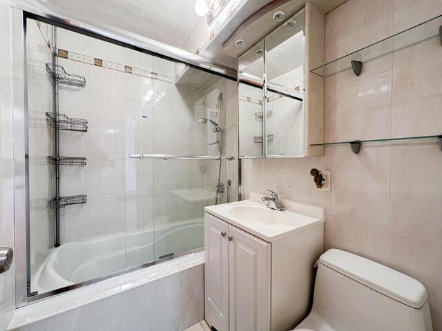 full bathroom with bath / shower combo with glass door, tile walls, vanity, toilet, and tile patterned floors