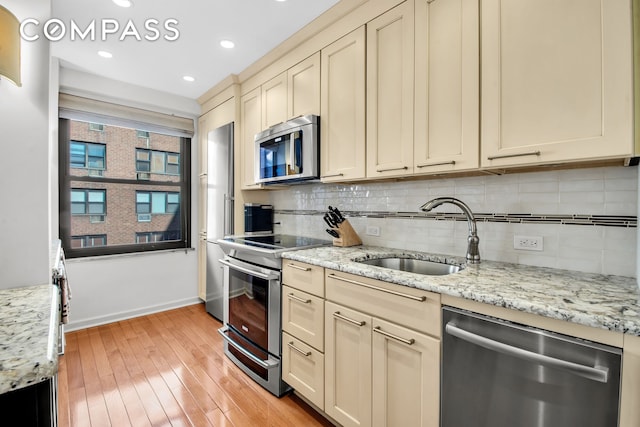 kitchen with backsplash, light wood-type flooring, cream cabinetry, stainless steel appliances, and a sink