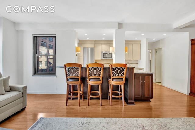 interior space featuring a breakfast bar, refrigerator, stainless steel microwave, light wood-type flooring, and backsplash