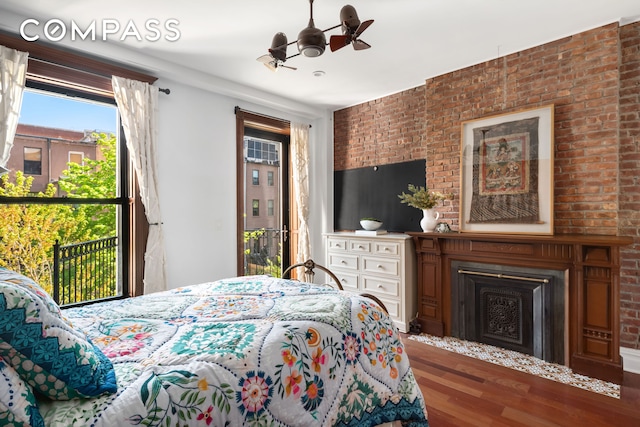 bedroom with a fireplace, brick wall, and wood finished floors