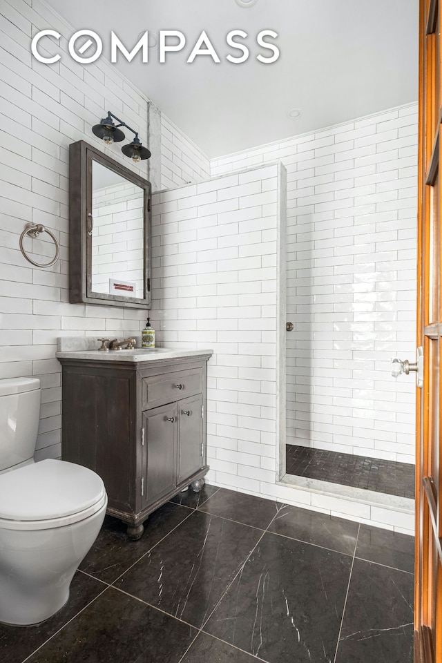 full bathroom with a tile shower, toilet, tile walls, and vanity