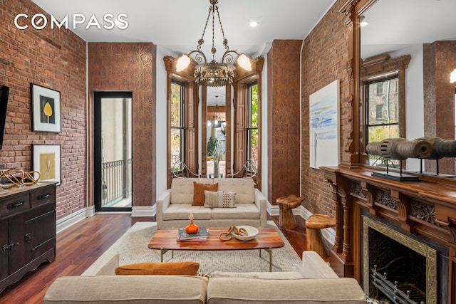 living area with dark wood finished floors, a fireplace, a notable chandelier, brick wall, and baseboards