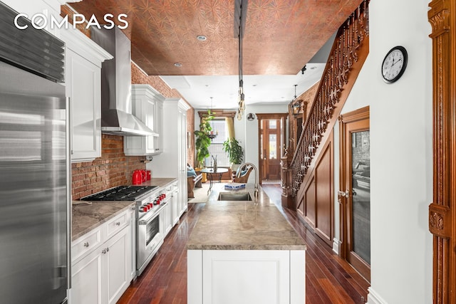 kitchen with white cabinets, premium appliances, dark wood-type flooring, wall chimney range hood, and a sink