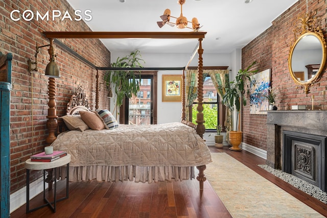 bedroom with a fireplace, brick wall, baseboards, and wood finished floors