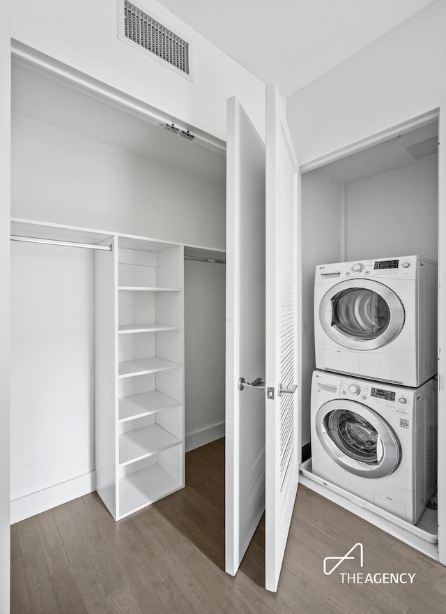 clothes washing area featuring laundry area, stacked washer and clothes dryer, visible vents, and wood finished floors