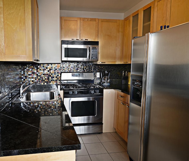 kitchen with light tile patterned floors, stainless steel appliances, a sink, backsplash, and glass insert cabinets