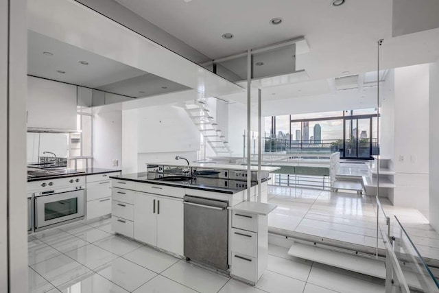 kitchen with wall oven, white cabinets, dark countertops, a sink, and stainless steel dishwasher