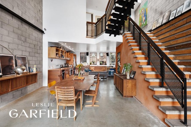 dining space featuring a high ceiling, stairway, and concrete flooring