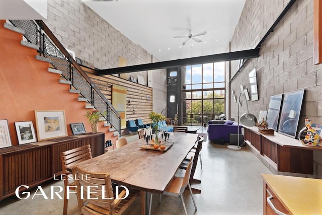 dining area with stairway, finished concrete flooring, a high ceiling, and a ceiling fan