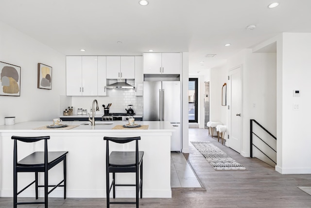 kitchen with a sink, wall chimney exhaust hood, a breakfast bar, and high end refrigerator