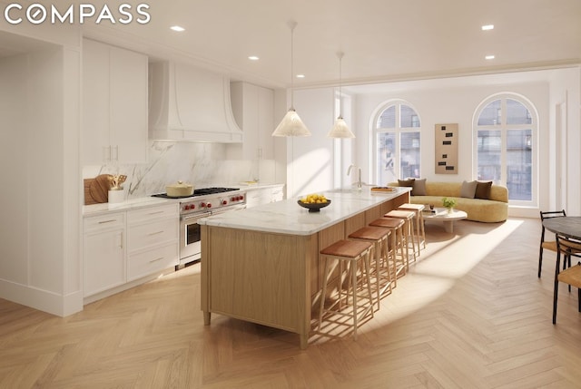 kitchen with a kitchen island with sink, premium range hood, white cabinetry, double oven range, and light stone countertops