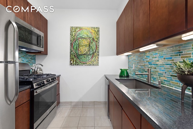 kitchen featuring a sink, dark stone countertops, backsplash, appliances with stainless steel finishes, and light tile patterned floors