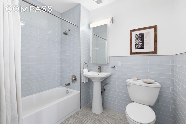 bathroom featuring wainscoting, toilet, tile walls, and shower / tub combo