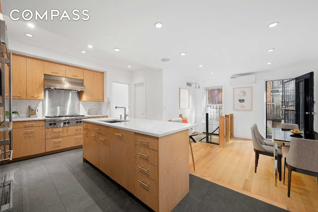 kitchen with sink, a kitchen island with sink, backsplash, an AC wall unit, and stainless steel gas stovetop