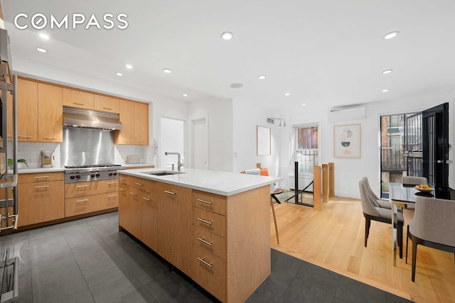 kitchen featuring tasteful backsplash, stainless steel gas cooktop, a sink, light countertops, and under cabinet range hood