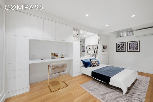 bedroom featuring light wood-style floors, an AC wall unit, recessed lighting, and built in desk