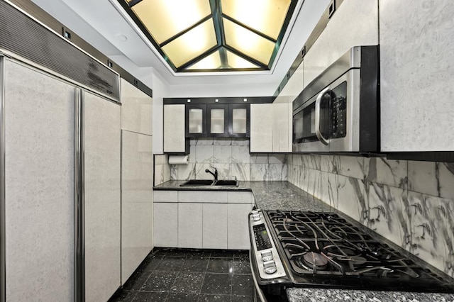 kitchen featuring appliances with stainless steel finishes, glass insert cabinets, white cabinetry, a sink, and dark stone counters