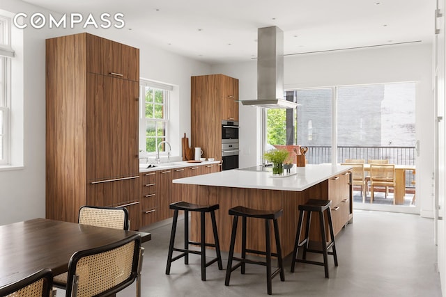 kitchen with island exhaust hood, concrete flooring, light countertops, and modern cabinets