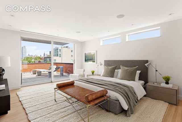 bedroom with a city view, light wood-style flooring, recessed lighting, baseboards, and access to exterior