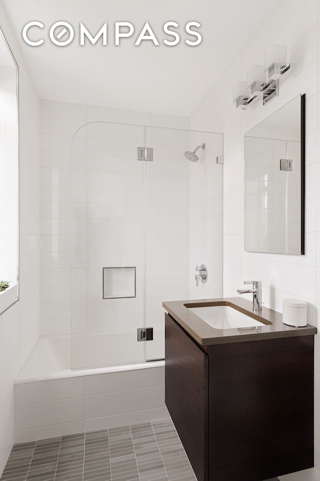 full bath featuring vanity, tile walls, and combined bath / shower with glass door