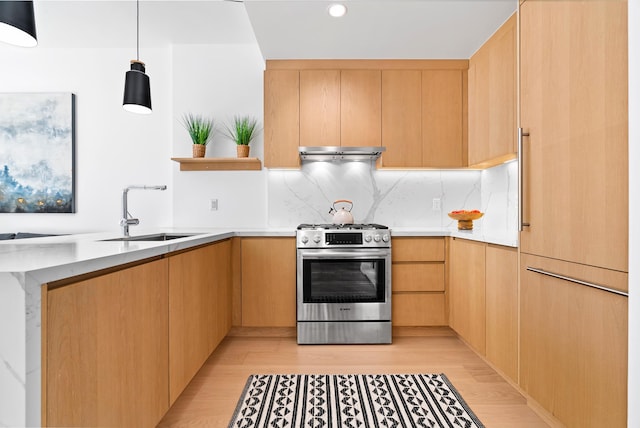 kitchen with a sink, under cabinet range hood, stainless steel gas range oven, light wood-type flooring, and backsplash