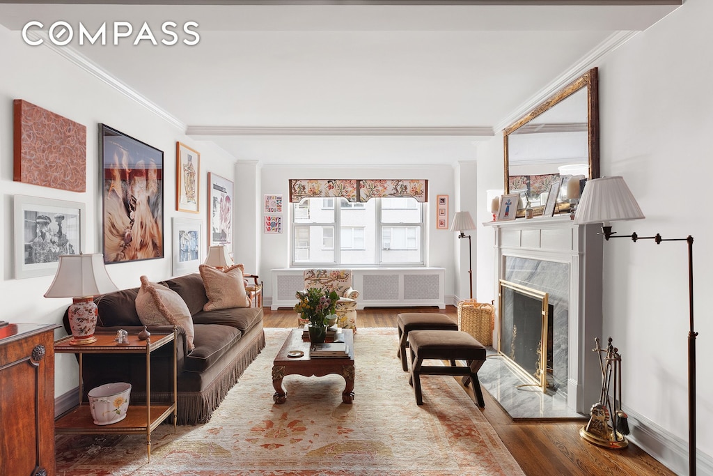 living area featuring a high end fireplace, baseboards, wood finished floors, and crown molding