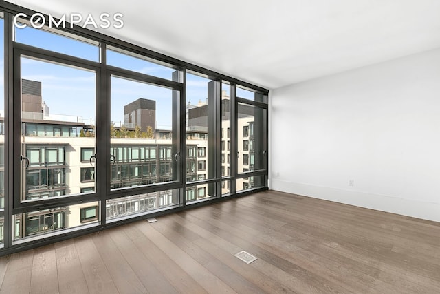 spare room featuring a city view, a wall of windows, wood finished floors, and baseboards