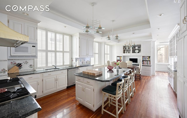 kitchen featuring dishwasher, a center island, a raised ceiling, and a sink