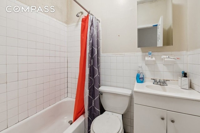 bathroom with toilet, vanity, shower / bath combo with shower curtain, wainscoting, and tile walls