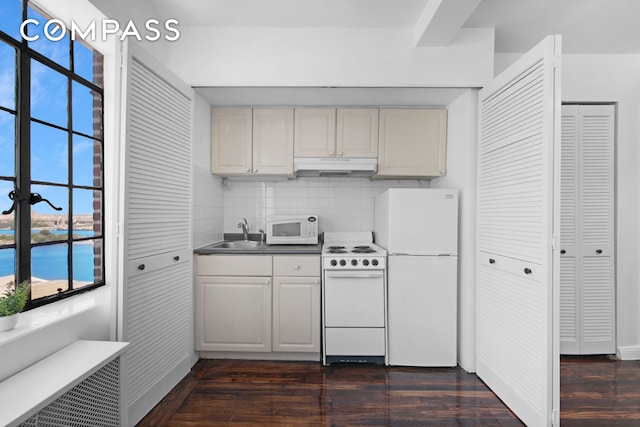 kitchen with under cabinet range hood, tasteful backsplash, dark wood finished floors, white appliances, and a healthy amount of sunlight