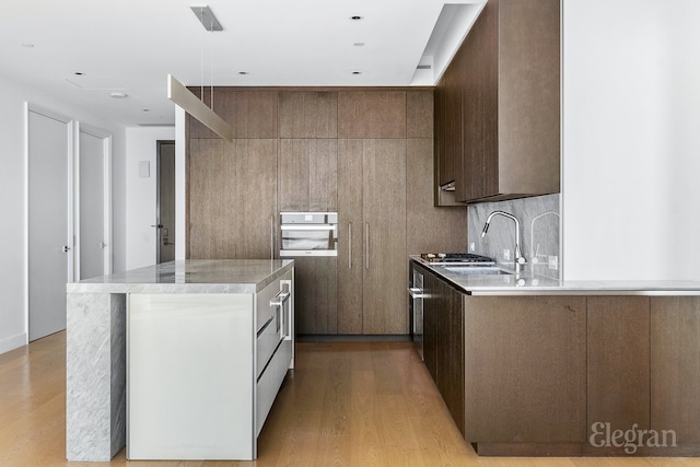 kitchen featuring light wood finished floors, modern cabinets, oven, a center island, and a sink