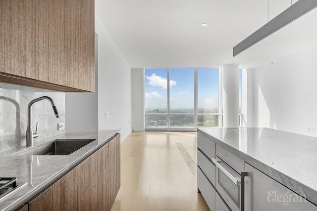 kitchen featuring modern cabinets, light stone counters, a sink, floor to ceiling windows, and backsplash