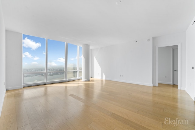 unfurnished room featuring expansive windows, baseboards, and light wood-style floors