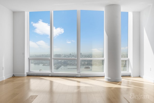 empty room featuring floor to ceiling windows, visible vents, baseboards, and wood finished floors