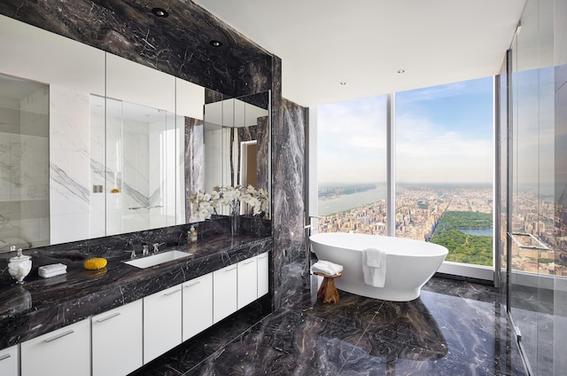 bathroom with marble finish floor, a freestanding bath, vanity, and stone wall