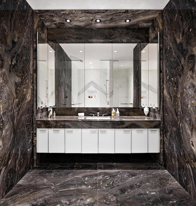 full bath featuring stone wall, recessed lighting, a sink, marble finish floor, and double vanity