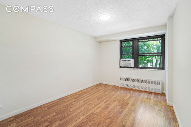 spare room featuring radiator, cooling unit, a textured ceiling, and light hardwood / wood-style floors