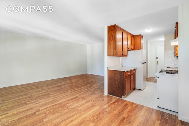 kitchen featuring light wood finished floors, light countertops, white appliances, and decorative backsplash