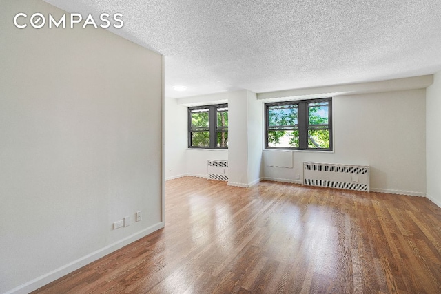 unfurnished room featuring wood-type flooring, radiator, and a textured ceiling