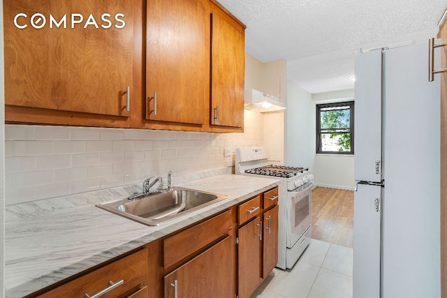 kitchen with sink, a textured ceiling, light tile patterned floors, white appliances, and backsplash