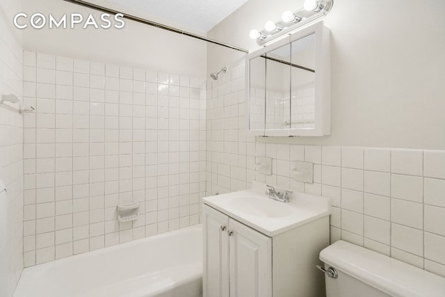 full bathroom with tiled shower / bath, tile walls, vanity, and toilet