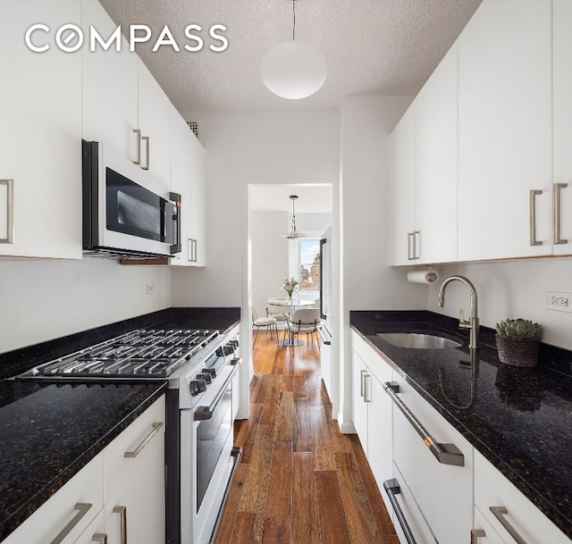 kitchen with gas range, white cabinetry, hanging light fixtures, and dark stone countertops